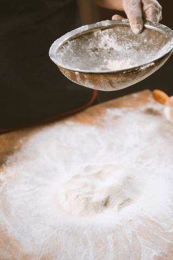 Baker pizza yapmak için un koyar. Şef ahşap bir masada kek pişirmek için hamur pişiriyor. Ev yapımı pişirme süreci. Makarna, ekmek, spagetti, khachapuri, yemek konsepti.