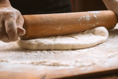 Şef masada merdaneyle hamuru yuvarlıyor. Eller yakın plan. Makarna, ekmek, spagetti, khachapuri, yemek konsepti.