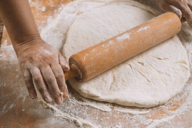 Şef masada merdaneyle hamuru yuvarlıyor. Eller yakın plan. Makarna, ekmek, spagetti, khachapuri, yemek konsepti.