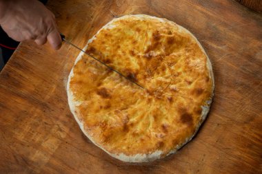 Ahşap arka planda ev yapımı etli turta kesen kişi. Bulgar banitsa, Gürcü khachapuri, Yunan tiropita