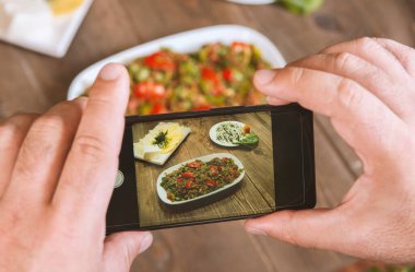 Yemek blogcusu akıllı telefon kullanarak fotoğraf çekiyor. Mans elleri geleneksel doğu yemeklerini telefonla çekiyor. Öğle ya da akşam yemeği. Sosyal medya ve blog için. Sağlıklı yemek.