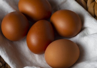 Beyaz havlu ve hasır sepette kahverengi yumurtalar. Üst manzara, düz uzanma