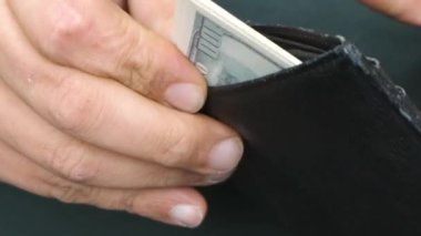 A man pulls out 100 dollar bills from his battered wallet.