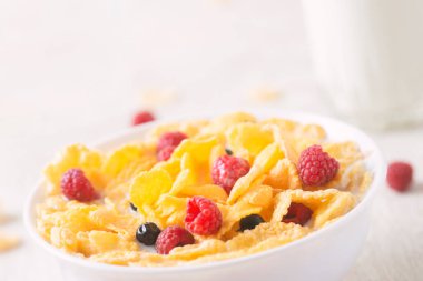 Böğürtlenli mısır gevreği, yabanmersini ve beyaz ahşap arka planda sütlü frenk üzümü.