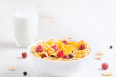 Bir kase mısır gevreği, sütlü, taze ahududu, yabanmersini. Sağlıklı kahvaltı için bir sürahi süt ve beyaz tahta üzerinde bir bardak.