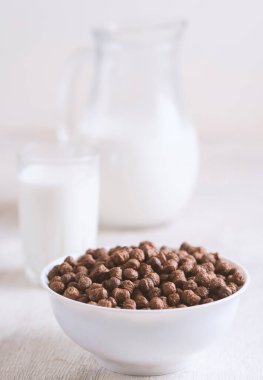 Beyaz ahşap arka planda çikolatalı mısır topu ve süt dolu bir kase..