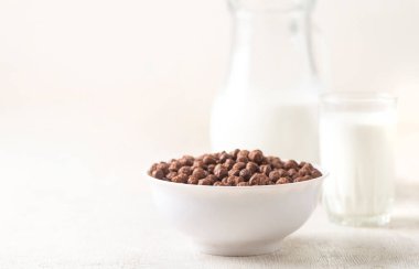 Beyaz ahşap arka planda çikolatalı mısır topu ve süt dolu bir kase..