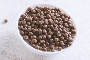 Beyaz ahşap arka planda çikolatalı mısır topu ve süt dolu bir kase..