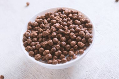 Beyaz ahşap arka planda çikolatalı mısır topu ve süt dolu bir kase..