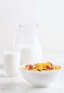 Mısır gevreği, yaban mersini ve ahududu ile sağlıklı kahvaltı. Sağlıklı mısır gevreği, beyaz masa üzerinde süt ve böğürtlen ile kase. Meyveli lezzetli yuvarlak mısır gevreği. Diyet kavramı.