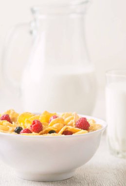 Mısır gevreği, yaban mersini ve ahududu ile sağlıklı kahvaltı. Sağlıklı mısır gevreği, beyaz masa üzerinde süt ve böğürtlen ile kase. Meyveli lezzetli yuvarlak mısır gevreği. Diyet kavramı.