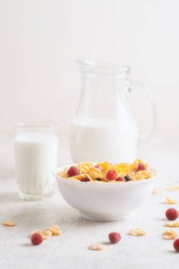 Bir kase mısır gevreği, sütlü, taze ahududu, yabanmersini. Sağlıklı kahvaltı için bir sürahi süt ve beyaz tahta üzerinde bir bardak.