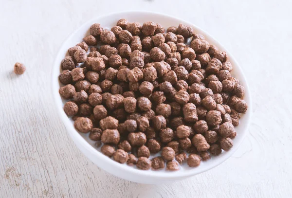 Beyaz ahşap arka planda çikolatalı mısır topu ve süt dolu bir kase..