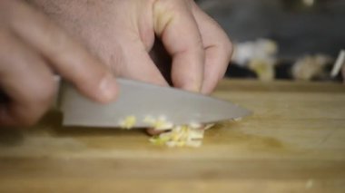 A man with a knife cuts garlic into small pieces .