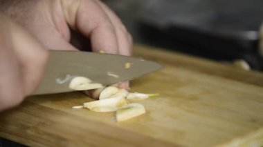 A man with a knife cuts garlic into small pieces .