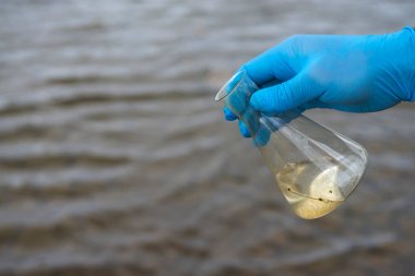 Analiz için nehirden örnek su. Bir test tüpü tutan eldiven. Ekoloji konsepti.