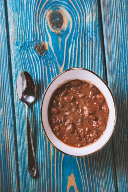 Beyaz kasede fasulye çorbası ve tahta masada kaşık. Üst Görünüm