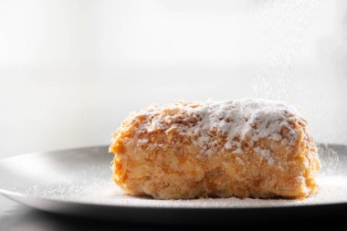 Siyah arka planda krema şekerli Napolyon keki. Napolyon kekini pudra şekeriyle süslemek.