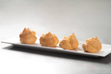 Profiterolleri pudra şekeriyle süslemek. Siyah arkaplanda krema şekerli ekler