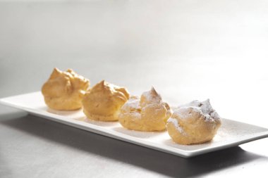 Profiterolleri pudra şekeriyle süslemek. Siyah arkaplanda krema şekerli ekler