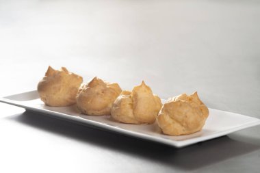 Profiterolleri pudra şekeriyle süslemek. Siyah arkaplanda krema şekerli ekler