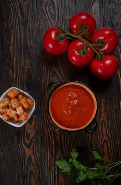 Kahverengi arka planda siyah bir kasede domates çorbası. Üst görünüm.