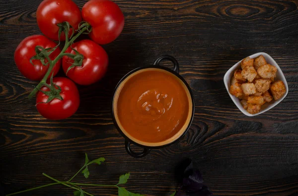 Kahverengi arka planda siyah bir kasede domates çorbası. Üst görünüm.
