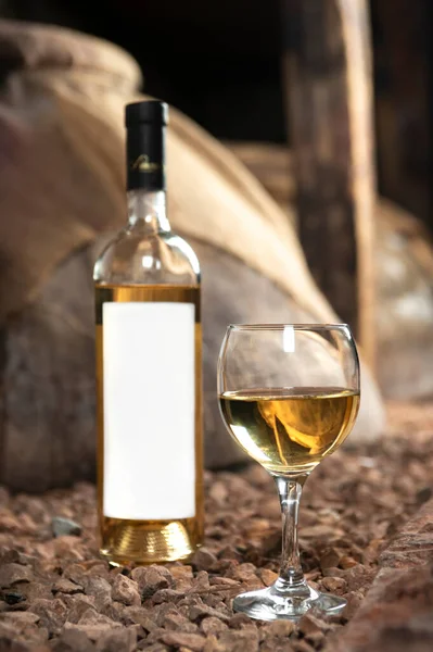 Glass and bottle of white wine in the wine cellar. Bottle with a label-preparation for designers