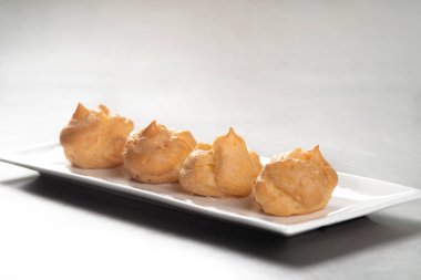 Profiterolleri pudra şekeriyle süslemek. Siyah arkaplanda krema şekerli ekler