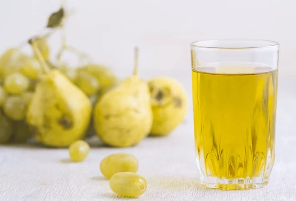 Juice of pears and grapes in a glass on a white wooden background