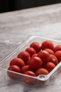 Tahta masadaki plastik kaplarda kiraz domatesleri.