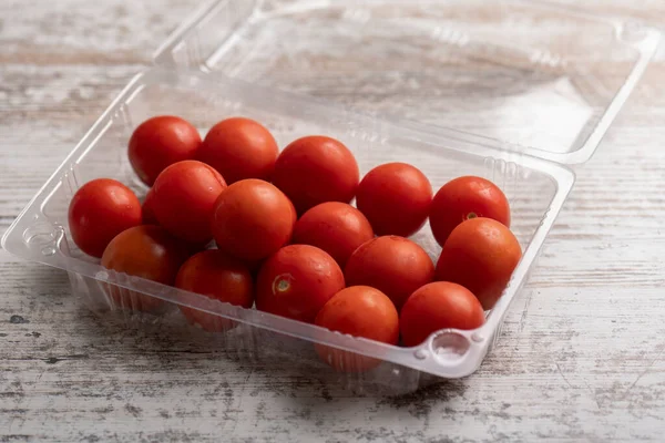 Tahta masadaki plastik kaplarda kiraz domatesleri.