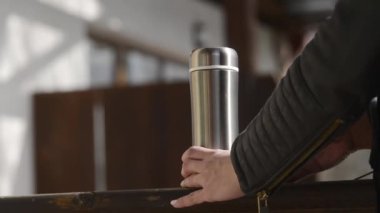 A woman opens a silver thermos with hot tea or coffee. vacation concept