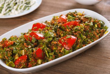 Bulgur, domates, maydanoz ve ahşap masadaki yeşil soğanlı Tabbouleh salatası. Geleneksel Ortadoğu ya da Arap yemeği.