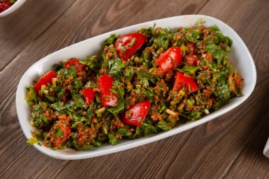 Bulgur, domates, maydanoz ve ahşap masadaki yeşil soğanlı Tabbouleh salatası. Geleneksel Ortadoğu ya da Arap yemeği.