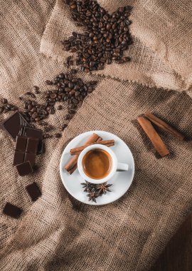 beyaz fincan kahve süt ve Aromatik baharatlar ile karanlık yol: tarçın, Yıldız anason, dilim limon ve kahve fasulye çuval bezi, peçeteye kurutulmuş