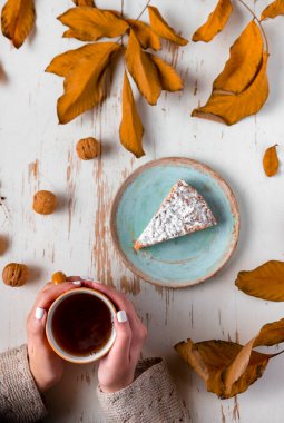 Sonbahar kompozisyonu, bir fincan kahve, bir dilim turta ve beyaz ahşap arka planda kuru yapraklar.