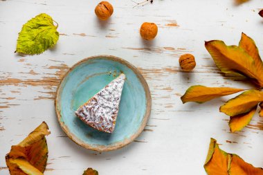 Sehpada servis edilen, dağınık yapraklı ve cevizli kek dilimi.