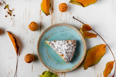 Sehpada servis edilen, dağınık yapraklı ve cevizli kek dilimi.