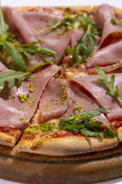 Jambonlu pizza, roka ve ahşap tabakta servis edilen şam fıstığı.