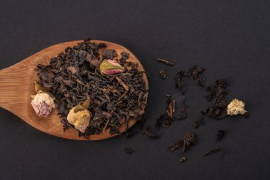 siyah arka plan üzerinde izole ahşap bir kaşık üzerinde gül çiçekleri ile aromatik siyah kuru çay