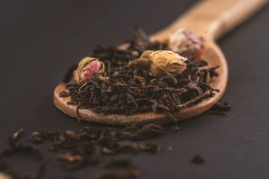siyah arka plan üzerinde izole ahşap bir kaşık üzerinde gül çiçekleri ile aromatik siyah kuru çay