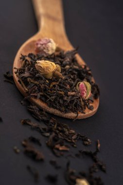 siyah arka plan üzerinde izole ahşap bir kaşık üzerinde gül çiçekleri ile aromatik siyah kuru çay