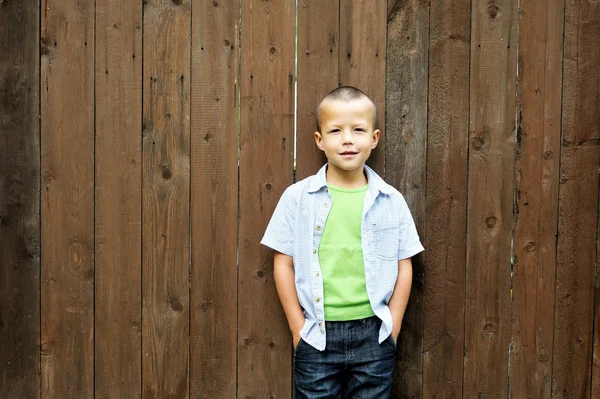 Kleine jongen poseren buiten in de buurt van houten hek — Stockfoto