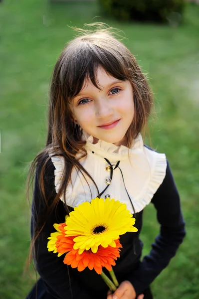 Jong meisje in schooluniform poseren met bloemen — Stockfoto