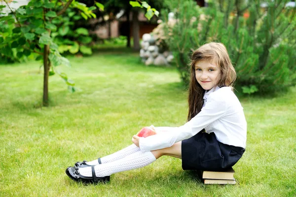 Jong meisje in school uniform zittend op boeken — Stockfoto