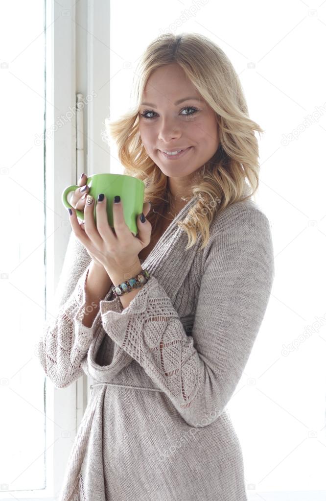Blonde girl at the window with a cup