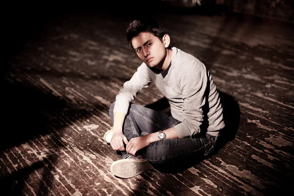 Ένας νεαρός άνδρας brunet που κάθεται σε ένα ξύλινο πάτωμα — Φωτογραφία Αρχείου