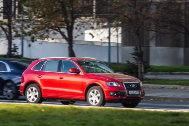 Moskova; Rusya - 14 Ekim 2021: Kırmızı Audi Q5, sıcak bir sonbahar gününde bir parkın arka planına doğru hızla ilerliyor.