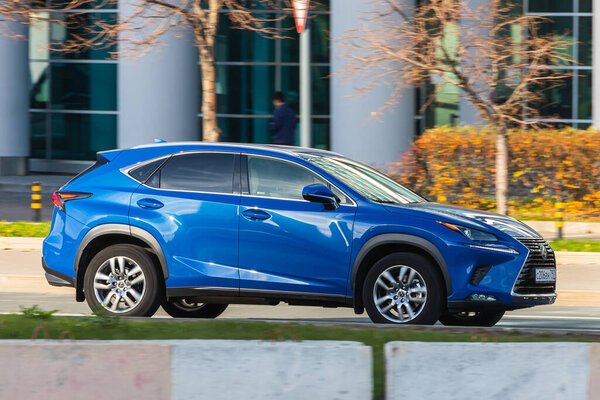 Москва; Россия - 14 октября; 2021: голубой Lexus NX быстро едет по улице в теплый осенний день на фоне парка